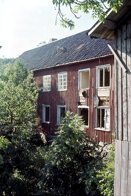 Nedeneshus. Saltrød gård. Rødmalt husvegg, hage og trær. Fotografert før riving.