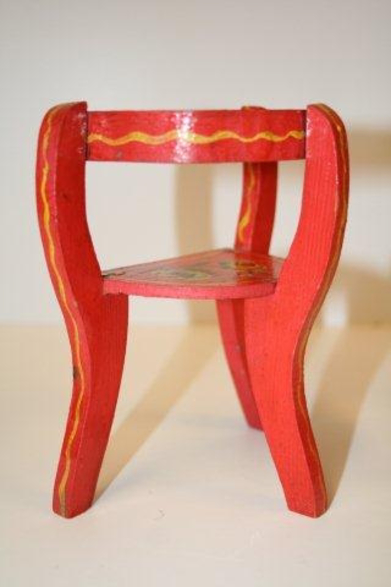 Trebeint stol. Halvsirkelformet sete av finér. Ben og stolper i étt. Kombinert armlene og ryggstøtte i metall som er malt som resten av stolen. Rødmalt  med blomsterdekor i gult, grønt, hvitt og blått. Streker og kanter er malt på. 
