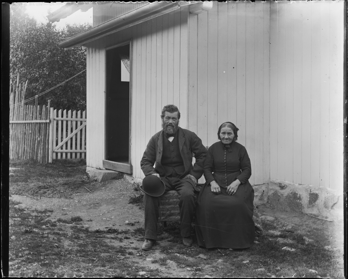 En mann og ei dame som sitter utenfor et hus.