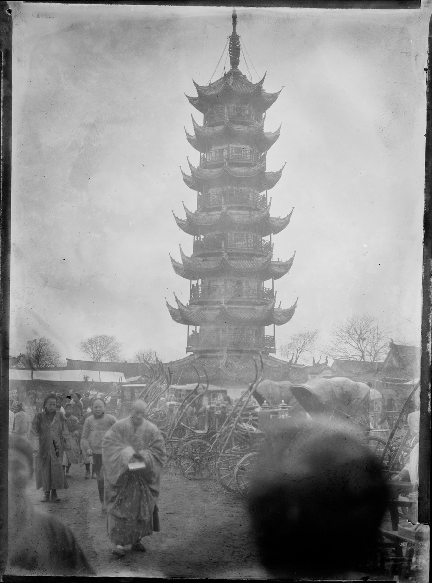 Et høyt tempel/tårn, trolig Langhwa pagoden i Shanghai. Flere mennesker av lokal befolkning i forgrunnen.