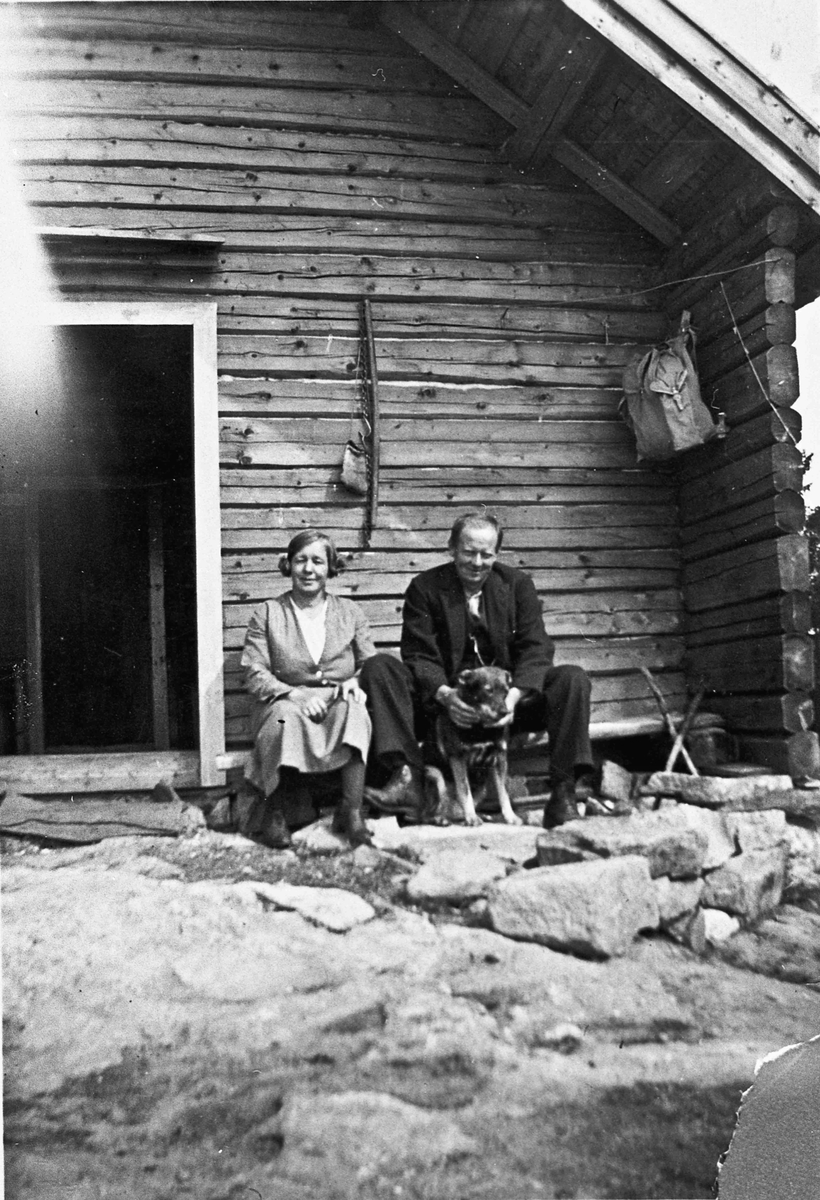 Kvinne og mann utenfor et tømmerhus.
