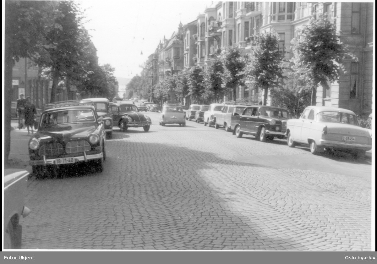 Nils Juelsgate. Brolagt gate med alle-trær. Folkevognen svinger ut fra Berens gate. Parkerte biler langs fortauskant på begge sider. Sannsynlig fra 1960-tallet.