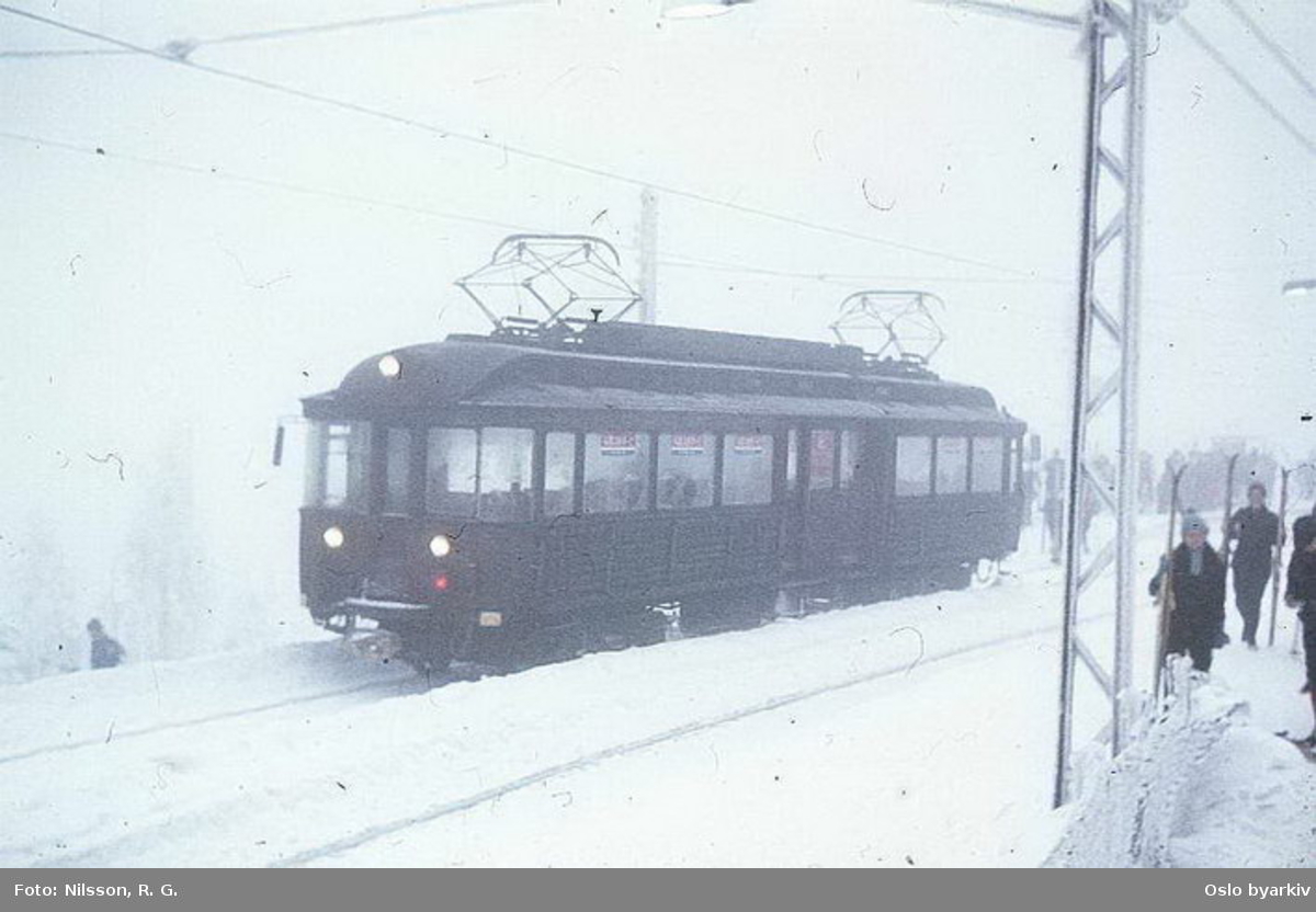 Holmenkollbanens vogn 112 ut fra ankomstplattform, snø og tåke på Frognerseteren stasjon.