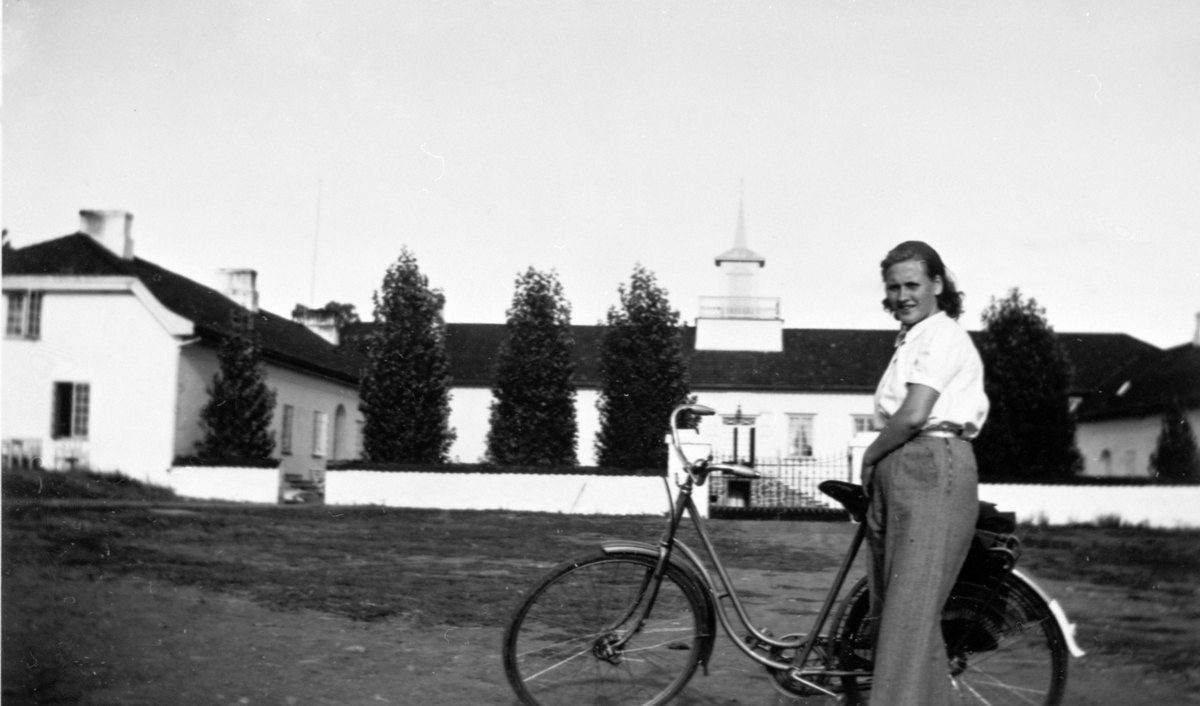 Anna Simensen (født Hatterud) med sykkel foran den nye hovedbygningen på Hovinsholm, Helgøya. Den gamle bygningen brant ned i 1937.