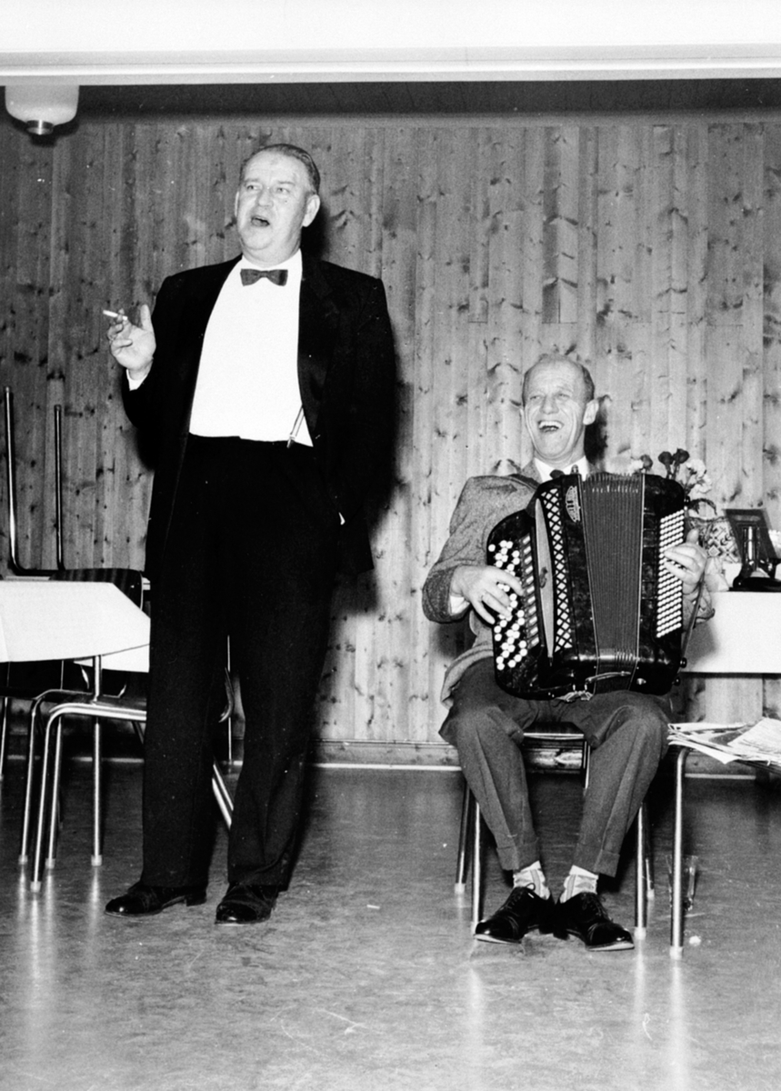 Alf Prøysen underholder på en familiekonfirmasjon, parodi på Ernst Rolf, trekkspiller til høyre.