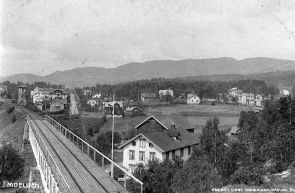 Postkort, Moelv sett fra jernbanebrua, i forgrunn til høyre er Brovold ned, Storgata.