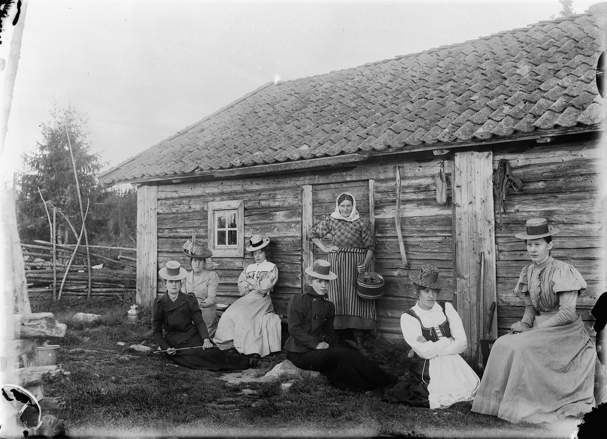Størhuset til Skraastad Øvre, Kluksetra i Vang allmenning. Syv kvinner i hytteveggen, kvinnedrakter, hatter,kjoler.