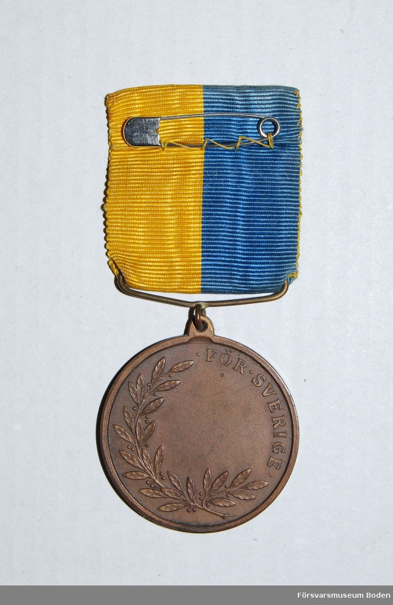 Med medaljband i blått och gult. Sköld med regementets vapen på åtsidan. Frånsidan har texten "För Sverige" med lagerkvist samt tom plats för namngravyr.