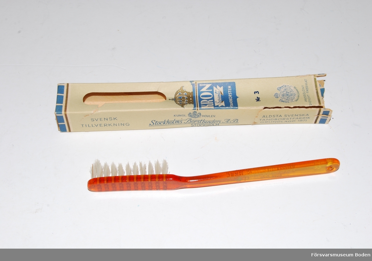 Oanvänd tandborste i öppnad och delvis defekt förpackning. Skaft av orange plast (celluloid) och borst av nylon. Troligen tillverkad mellan 1959-1966.