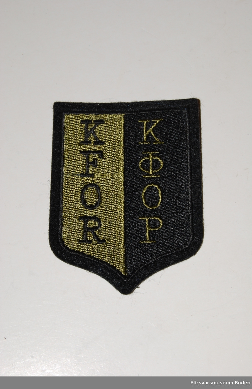 Broderat textilmärke, svart och olivgrönt. KFOR står för Kosovo Forces och är även skrivet med kyrilliska tecken. Märket bars av fredsbevarande enheter i Bosnien 1999-2007.