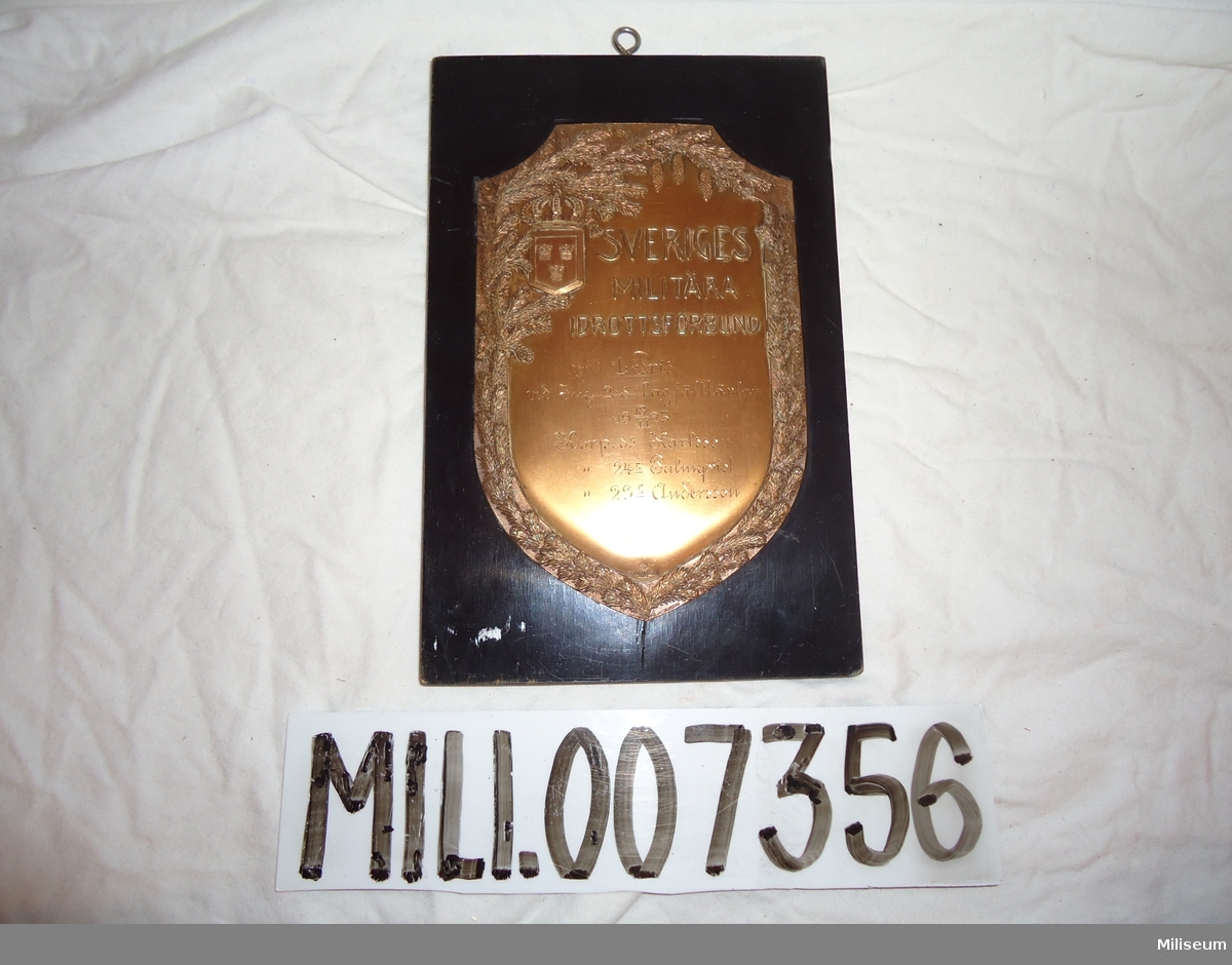 Prissköld av bronserad mässing, uppfästad på träplatta. "1:pris vid Ing 2:s lagfälttävlan 19 18/11 23."