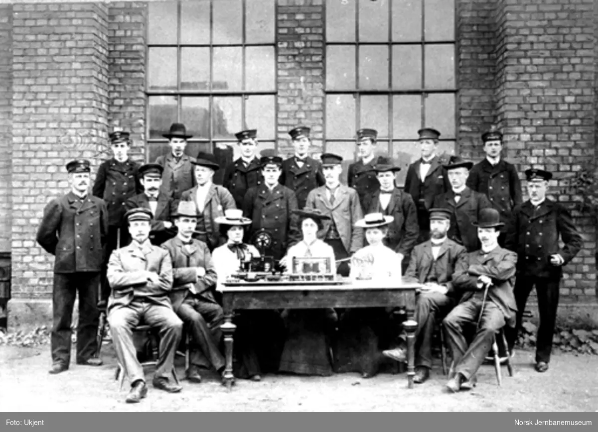Gruppebilde med 22 telegrafistelever bak et bord med telegrafiapparater