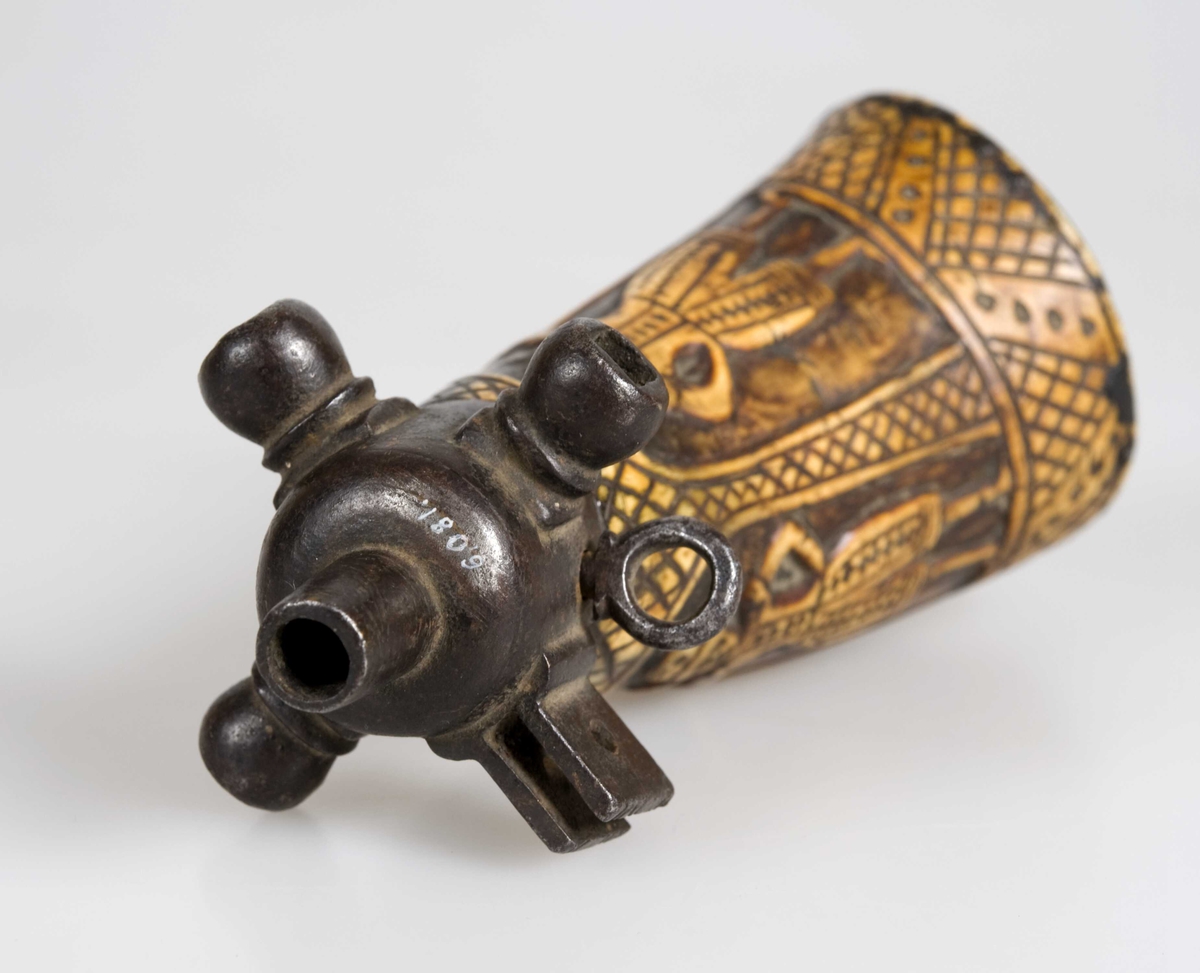 Krutthorn med figurer utskåret i relieff. Endestykket i jern har nøkler for å spenne geværlåsens hane.
