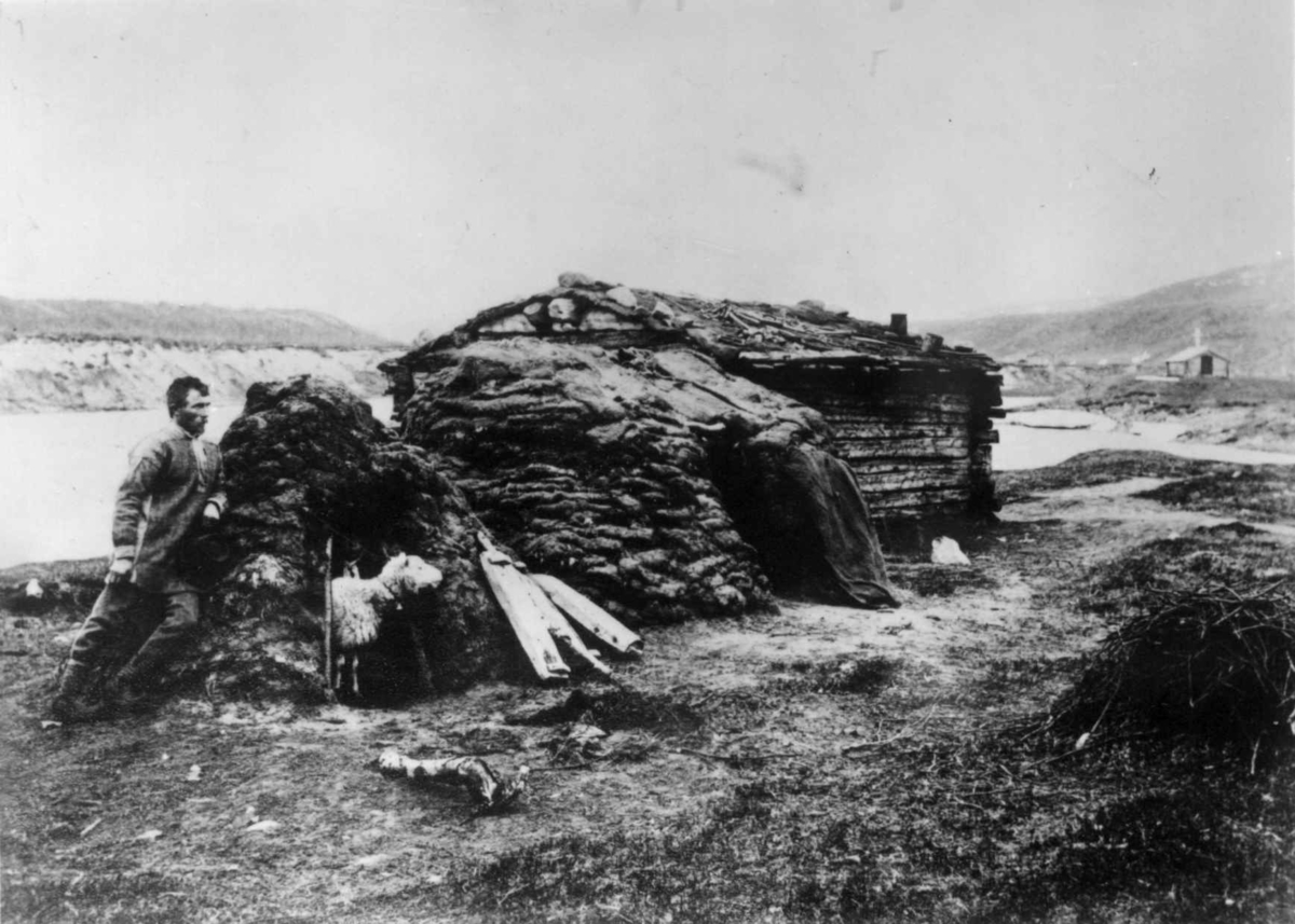 Skoltesamisk hus med fegamme, Neiden, Sør-Varanger, Finnmark,     ca. 1905. Mannen utenfor er Miket Ivanowetsj (1876-1916).