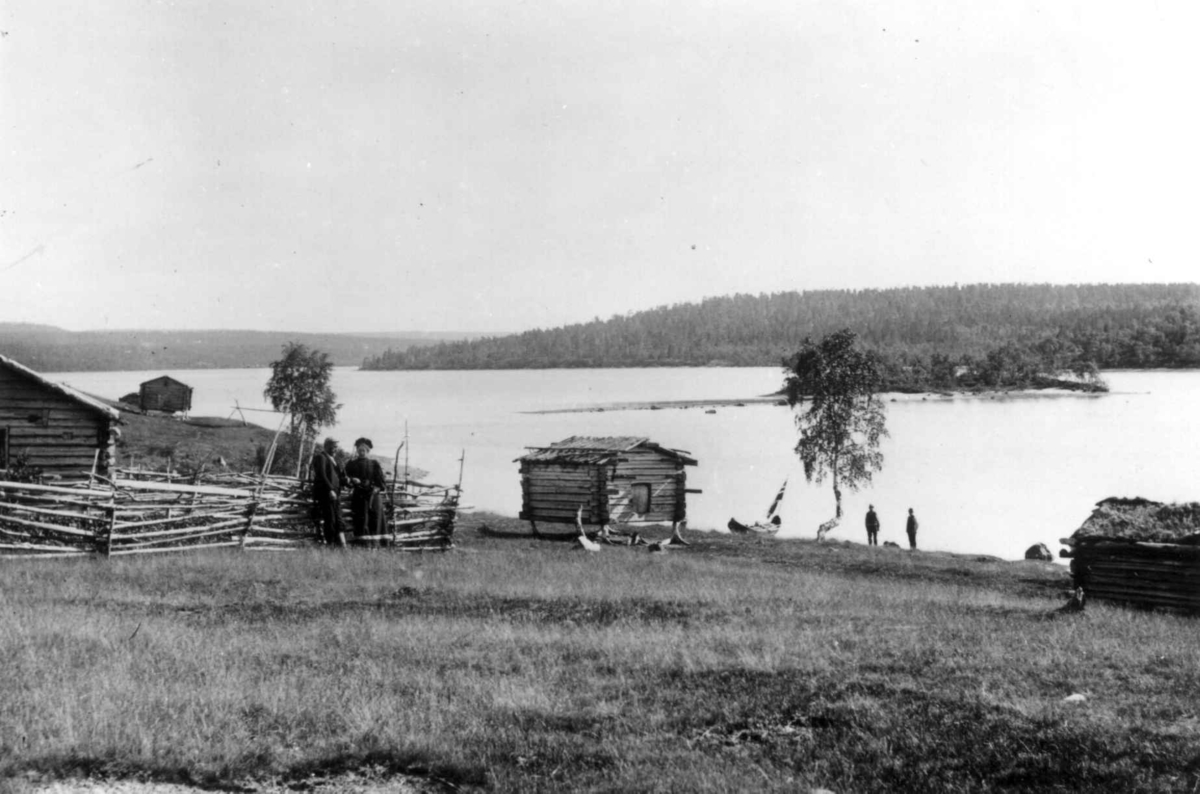 Skolteboplass på Nakholmen, Vaggetem, Finnmark, før 1900. Stabbur ved Pasvikelven. Ellisif Wessel ved gjerdet.