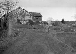 En dame går på en landevei med gårdbruk i bakgrunn, Kråkerøy