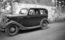 Voksne og barn sitter i Ford Junior 1936-modell. Antakelig K