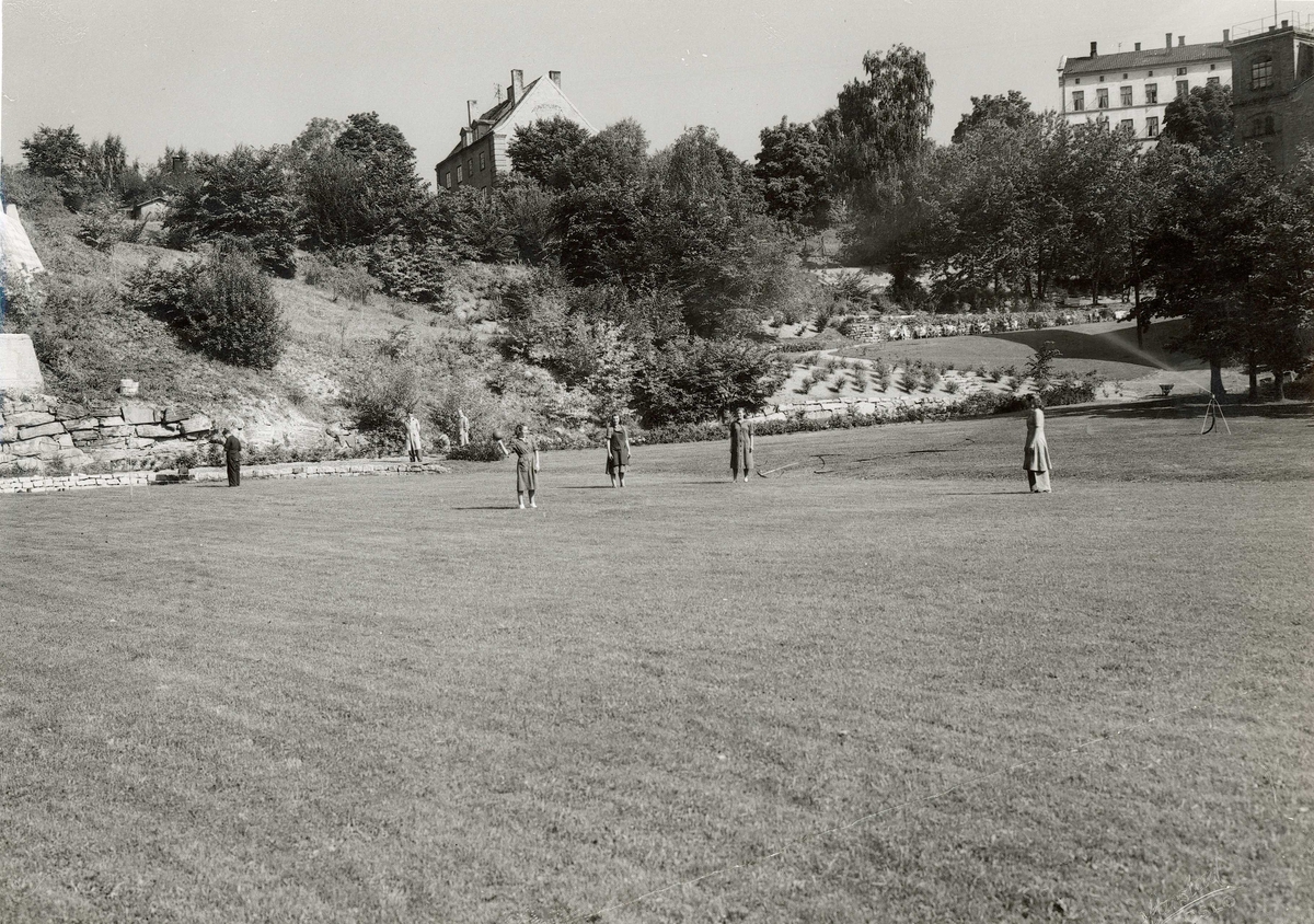 Fire kvinner kaster ball i parken til A/S Joh. Petersens Linvarefabrik. Tre menn står i bakgrunnen.