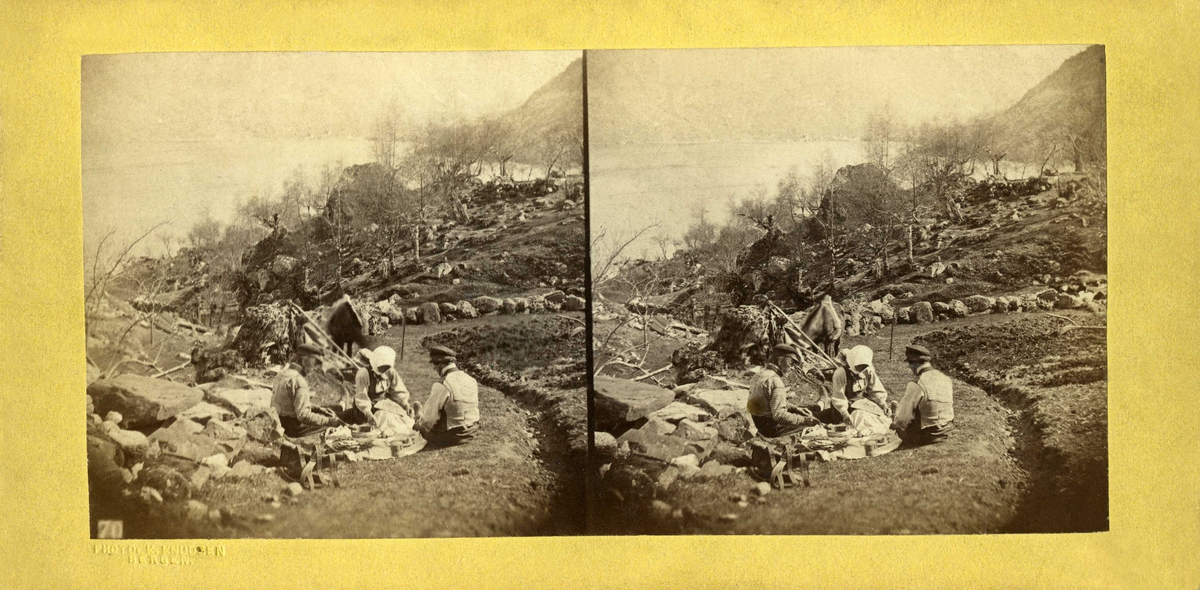 Antakelig fra Tokheim ved Sørfjorden i Hardanger. Stereoskopi fra perioden 1864-1880. "Middagsmaaltid i Saatiden". Tre personer sitter og spiser på bakken i et fjord- og fjellandskap.