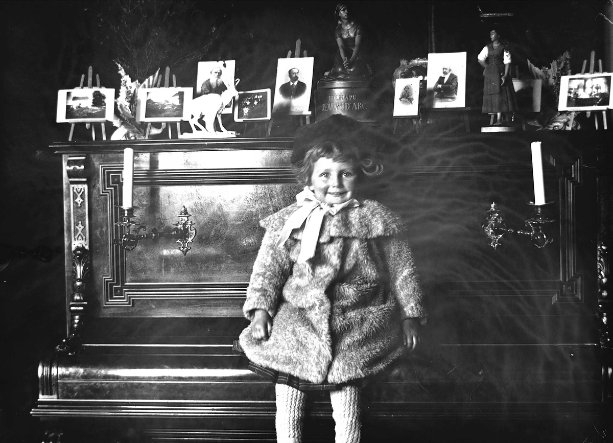 Gudrun Q. Wiborg sitter på pianolokk i Meltzers gate 9, Oslo, 1899. Fotografier i ramme plassert på pianoet.