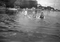 To kvinner og tre barn bader i sjøen med badedrakter og bade