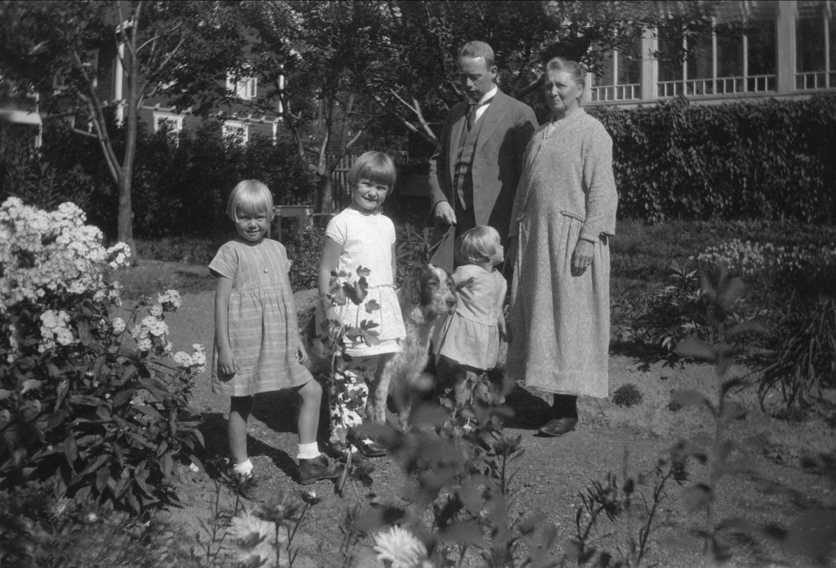 En gruppe mennesker poserer med en hund i en hage. Robsahm og Lund.