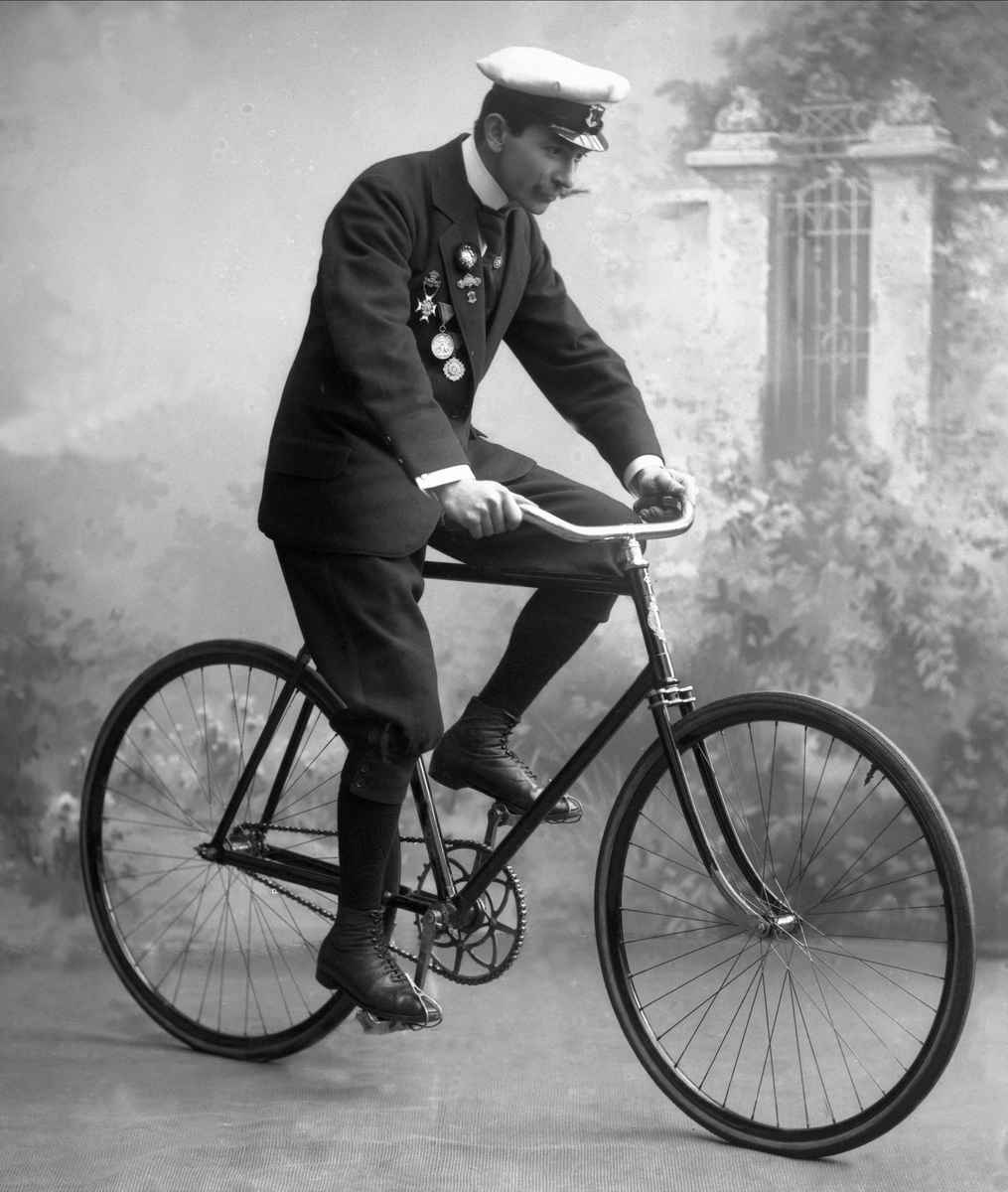 Portrett, mann med uniformslue, medaljer og sykkel.