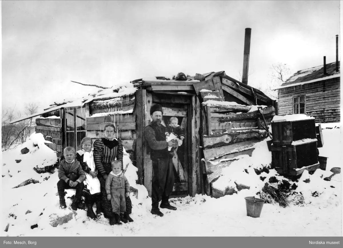 Familjen Söderberg i Kiruna framför sitt hus av kasserade bräder, isolerat med fjälltorv. Kiruna Söderberg, gruvsamhällets förstfödda, i sin fars armar.