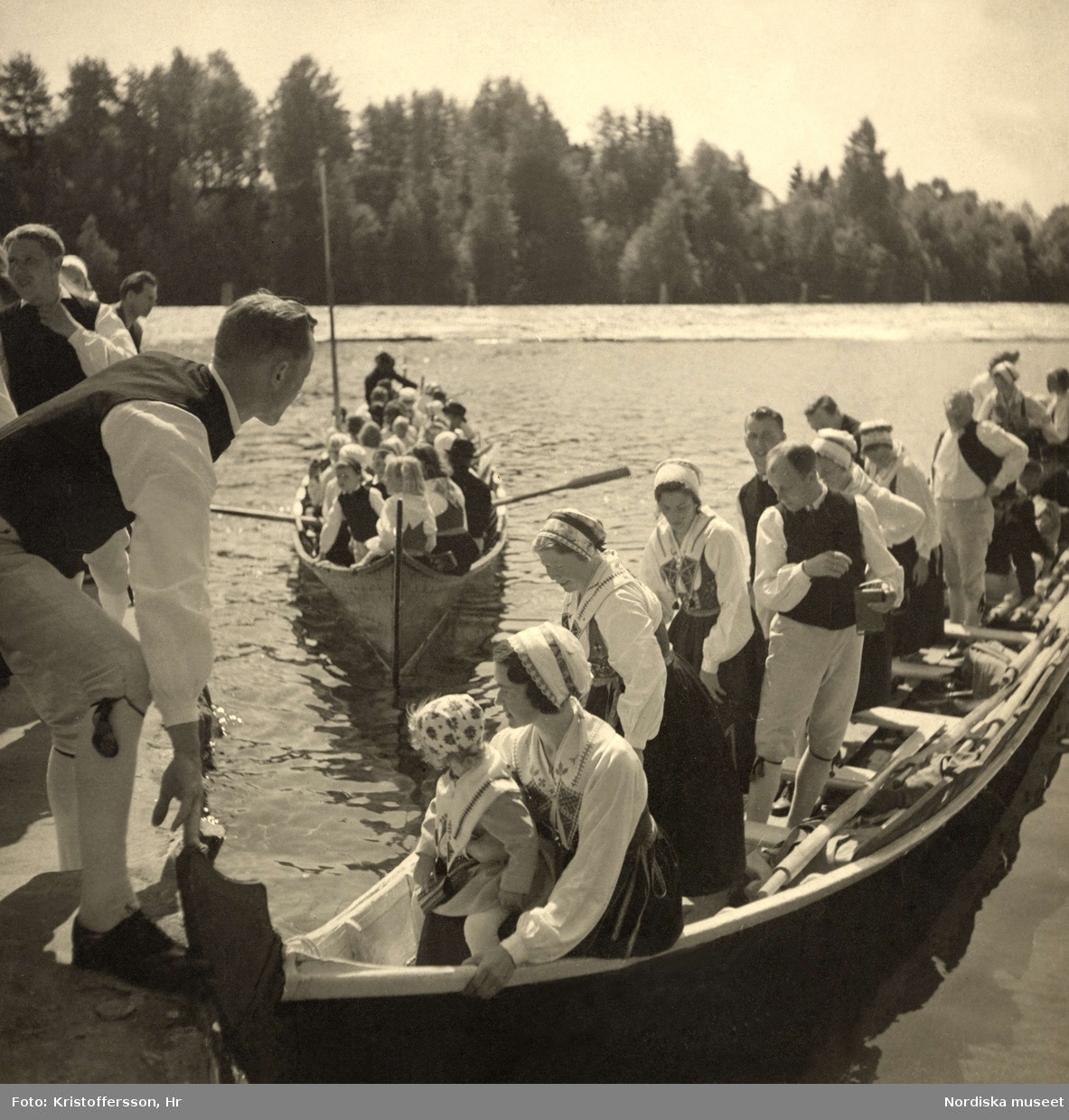 Kyrkbåtar i Leksan vid midsommar. Män, kvinnor och barn klädda i folkdräkter från Dalarna.