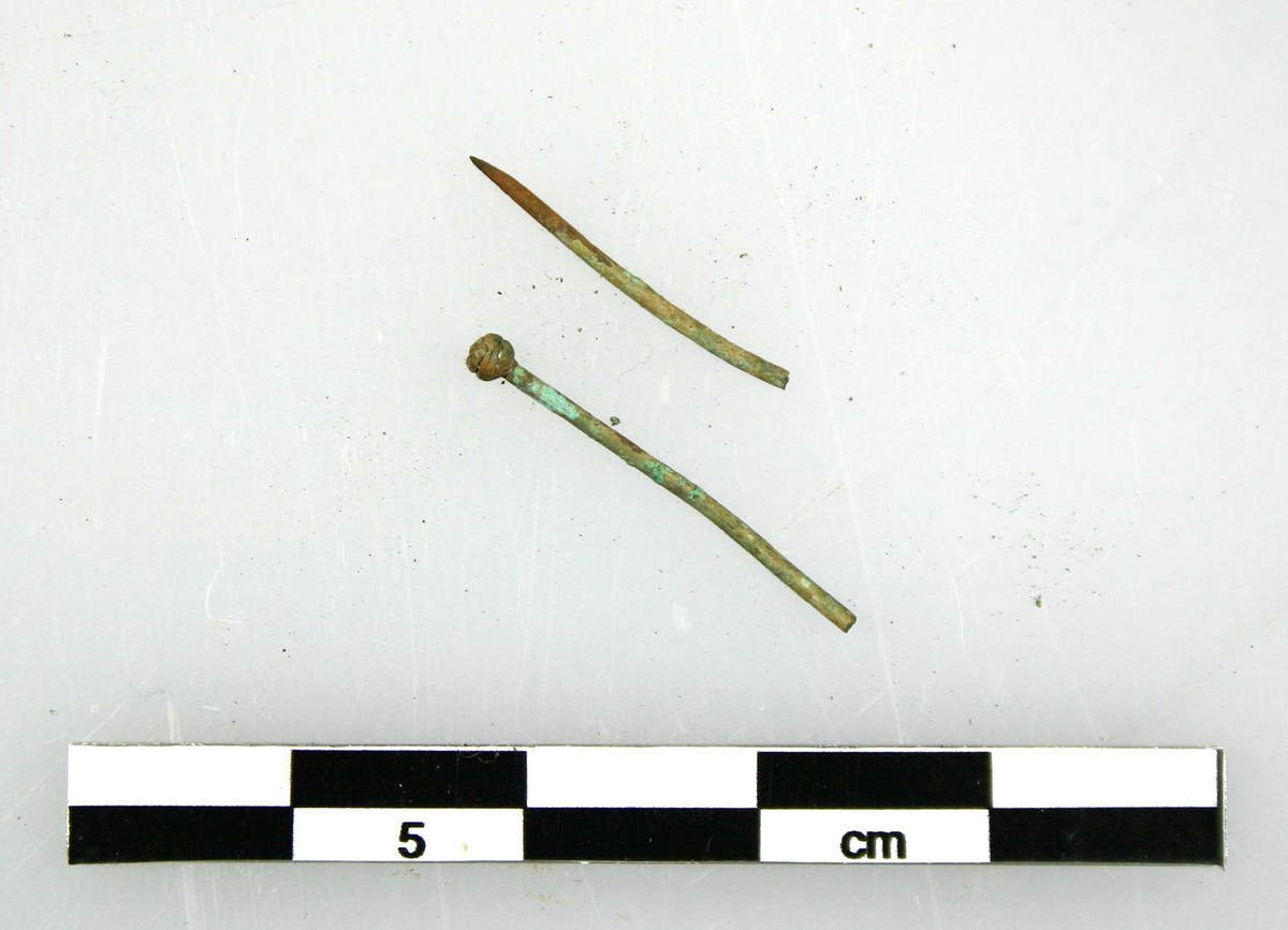 Två delar av nål, av brons. Kulformat huvud av bronstråd. Spiralvriden.
