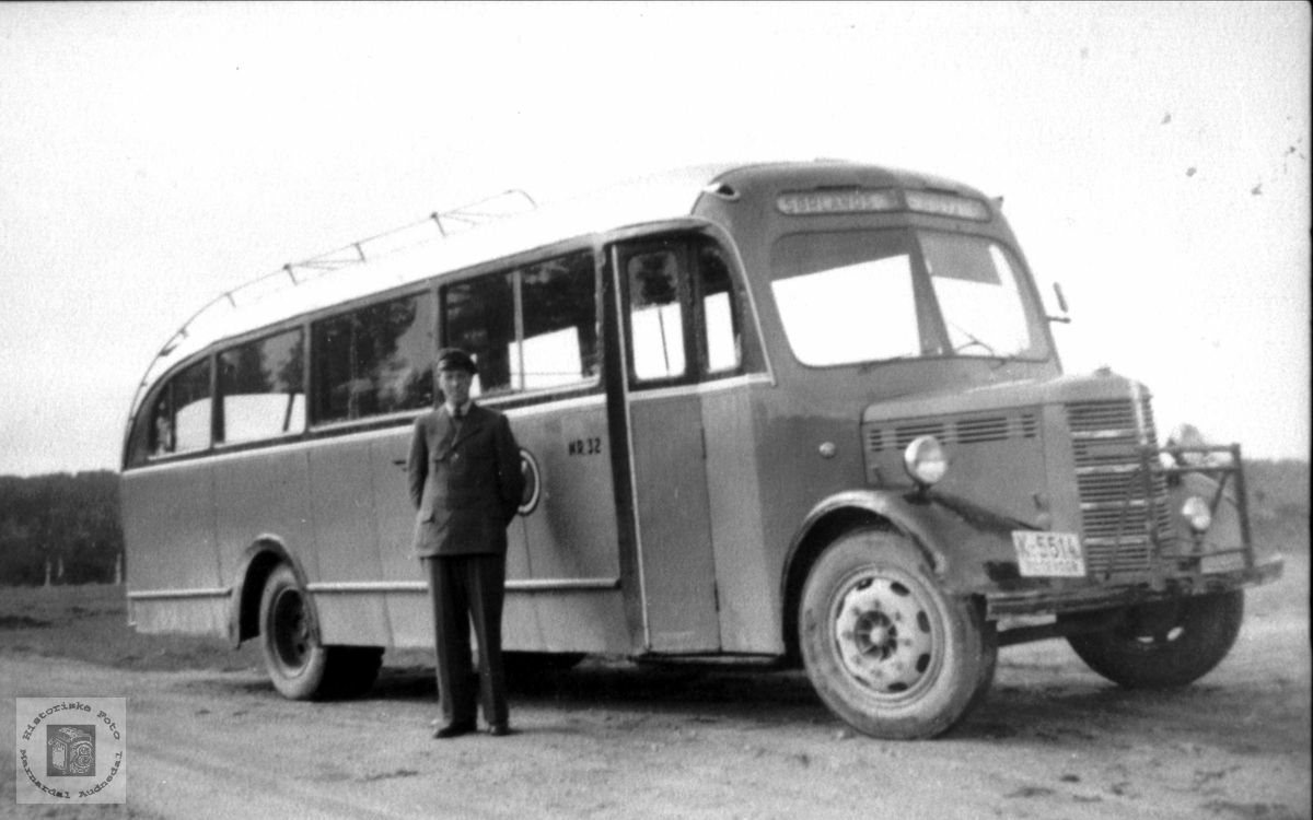 Portrett av sjåfør Karls Steinsland med bussen, Laudal.
K-5514 var en Bedford 1949-modell personbuss. Den ble levert ny til A/S Mandal og Oplands Automobilselskab. Dette selskapet ble i 1951 slått sammen med flere andre, og det nye selskapet fikk navnet Sørlandsruta. Denne bussen ble med over dit. Bildet er nok tatt etter fusjonen. Logoen til Sørlandsruta kan skimtes på siden bak sjåføren. Bussen hadde bensinmotor som ny, men fikk seinere dieselmotor.