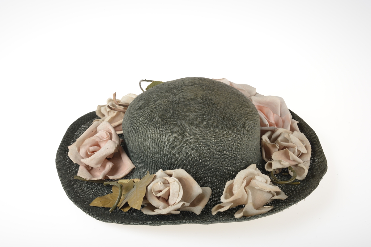 Hatten har rund pull med vid brem som er pyntet med stoffroser og blader.  Det er lagt inn en metallstreng ytterst i bremmen.