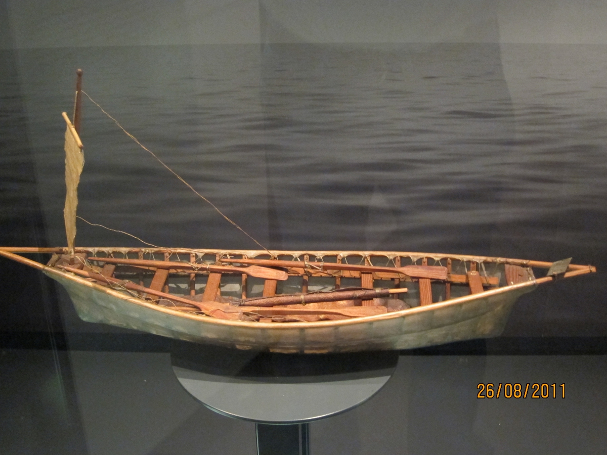 Skinnbåt på ribbeverk av tre, liten mast m. firkantet seil, endel utstyr.