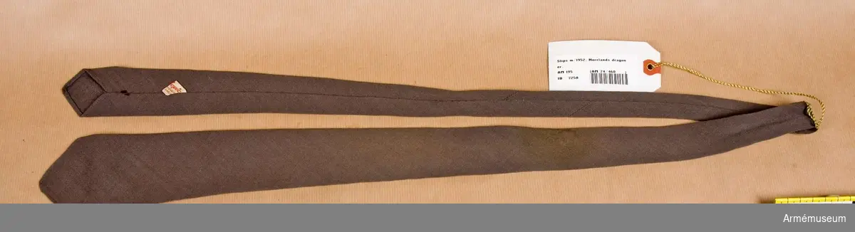 Slips tillverkad av ljusare gråbrungrönt ylletyg med sned skärning och dubbelvikt.
