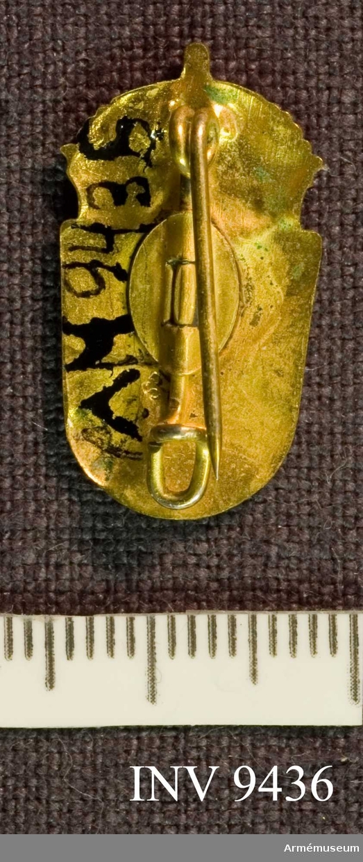 Samhörande nr är 9421 - 9438.
Civilförsvarsmärke i guld, SLK.
Ett förgyllt märke, troligen tillverkat hos Sporrong. Ingen märkning finns synlig. Framsidan visar två korslagda värjspetsar vilande på en sköld, krönt av en kunglig krona.