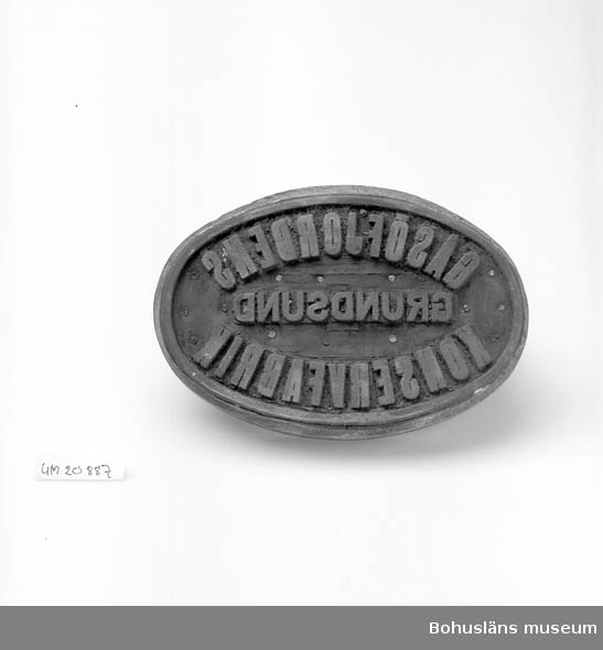 Oval trästamp med handtag, tryckplatta i gummi med texten: "Gåsöfjordens Konservfabrik, Grundsund". Använd till silltunnor och dyl.