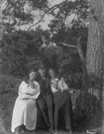Enl. text i blå bok: "Man och tre damer vid träd."