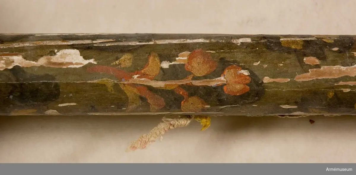 Stångens övre del bemålad med blomornament på mörkblå botten. Äpple med guldspår och konturer av bladornament. Nedre delen av stången målad i gult.
Påklistrad lapp med uppgift om att fanan tagits i Narva 1700.