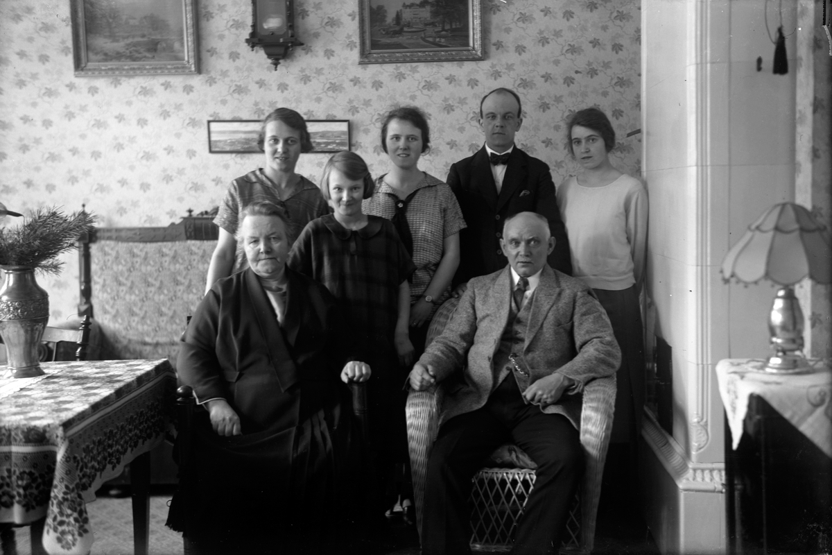 En kvinna och en man sitter i varsin stol. Bakom dem står en yngre man och fyra unga kvinnor.