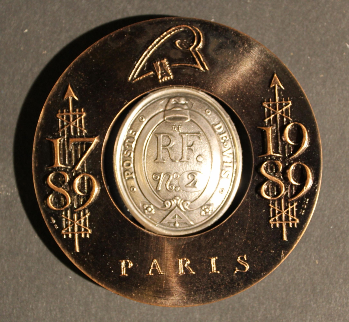 Medalj i brons och silver. Medaljen består av två delar,
denyttre är cirkulär och i brons, i dess mitt är ett cirkelformat
hål. Ihålet är en medalj med form av en "vapensköld" i silver
placerad.