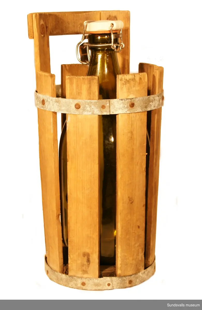 SuM 4961:1-2 två flaskor med patentkork och  korgar i trä med metallband. SuM 4961:1 är tillverkad i gröntonat glas. På korken står 'KLASS 1' i relief. Flaskan är 36,5 cm hög och bärdonet 40 cm. SuM 4961:2 är tillverkad i bruntonat glas och har en kork märkt 'A.-B. KUMLA FRUKTINDUSTRI'. Flaskan är 43,5 cm hög och den rödmålade korgen mäter 40 cm på höjden.