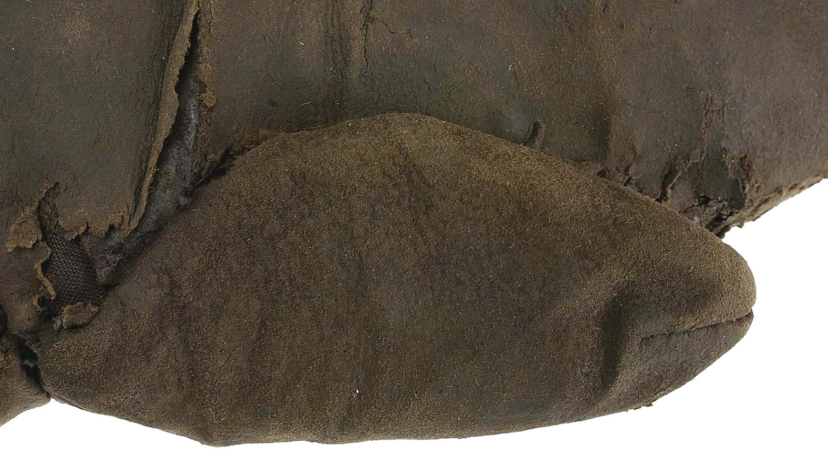 En kragvante till höger hand. Sydd av flera kraftiga läderstycken. Påsydd bård i ett stycke i form av rundade "tungor" längs kragkanten.
