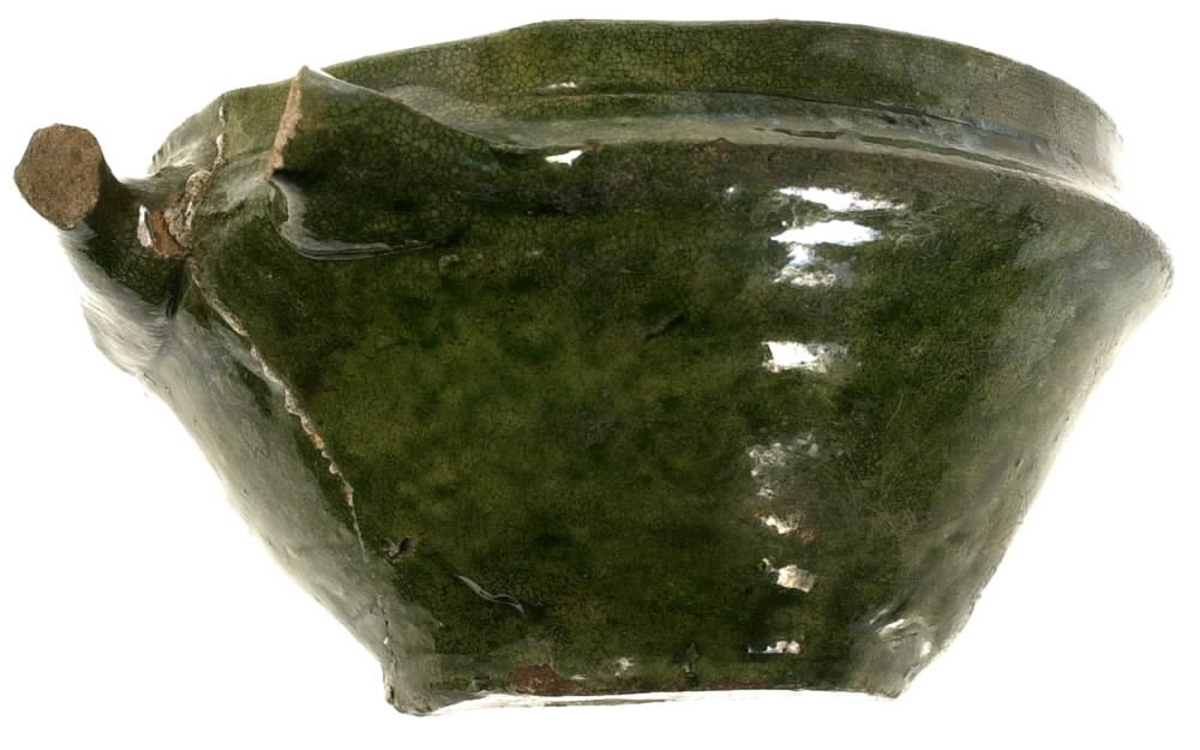 Del av en keramikskål. Skålen är tillverkad i vitbränt lergods. Skåldelen är försedd med en avbruten hänkel och utgör ena halvan av den ursprungliga skålen. Utsidan är glaserad med en grön glasyr och insidan med en senapsgul glasyr.