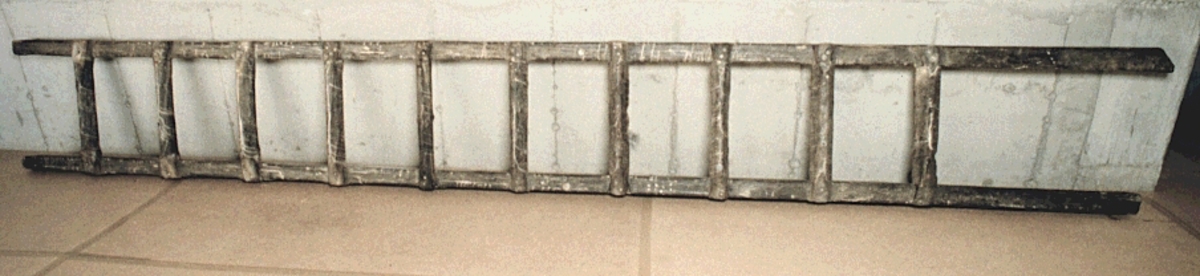 Trappsteg.
Triangulärt tvärsnitt. Framsida och underkant fasade. Laxstjärtformade ändar fästade vid varsin vang med två skruvar. Eroderat.