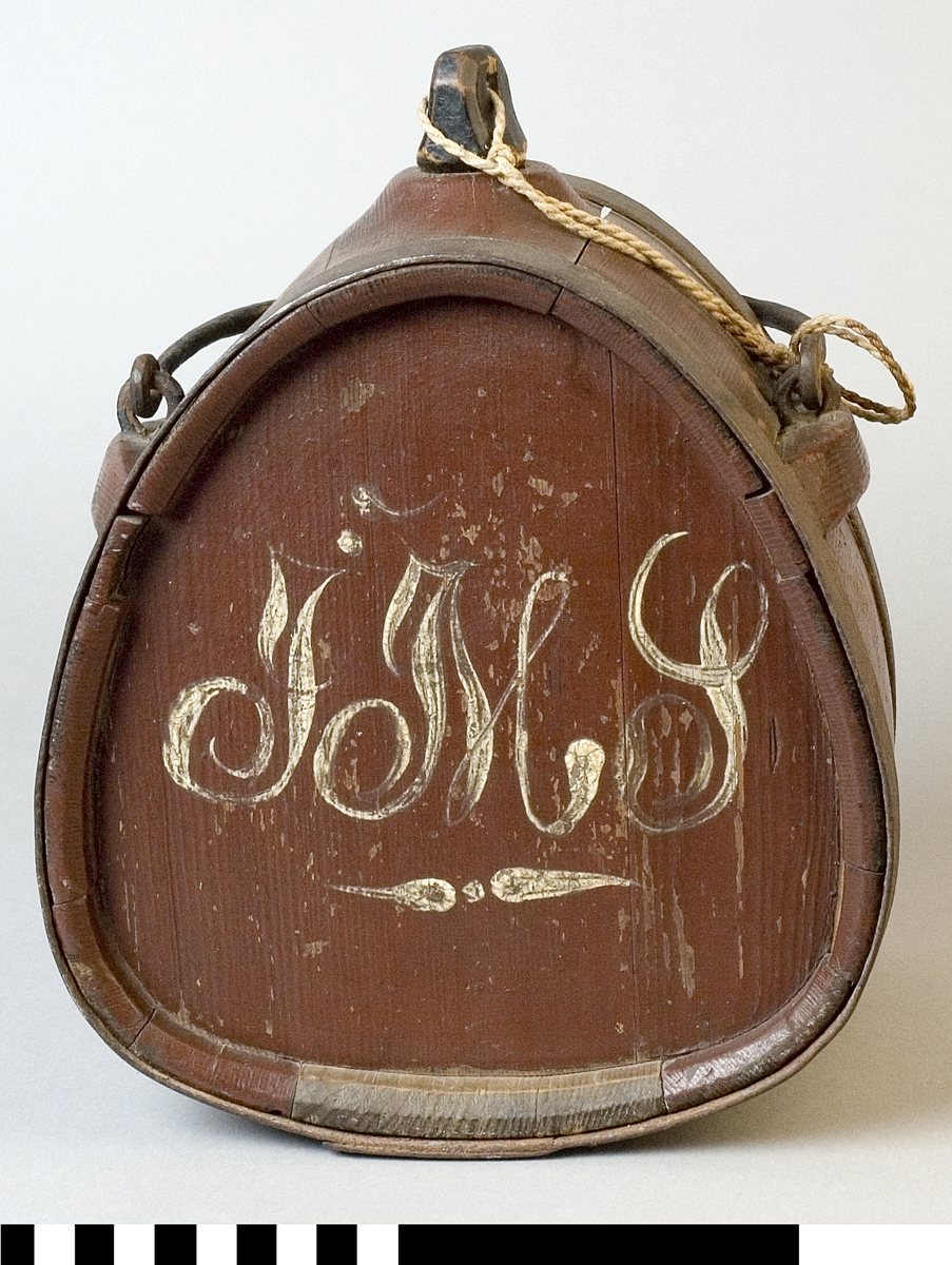 Mjölkflaska av trä, målad brun. Med band och handtag av järn. Med tillhörande propp av svartmålat trä. 
Märkt på ena sidan 1883, i vitt.
Märkt på andra sidan "JMS", i vitt.