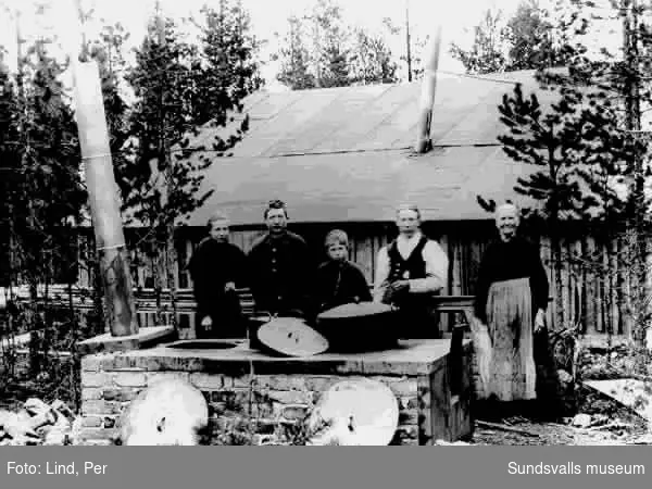 Alby 1898. "Ångköket". Gruppbild med tre vuxna och två barn som lagar mat.  Stor vedspis för utomhusbruk i bakgrunden ett trähus.