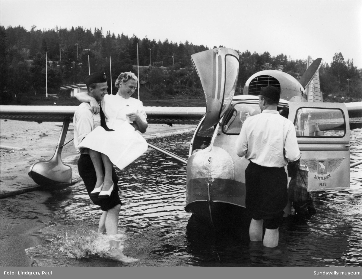 Gunnar "Spökis"  Andersson, pilot på denna ambulansflygning. På bilden ses brandmännen Mats Eriksson och Nils Stenlund. Sköterskan som bärs till planet heter Stina Hahne (avdelningssköterska vid operationsavdelningen på Sundsvalls sjukhus). Platsen är okänd.