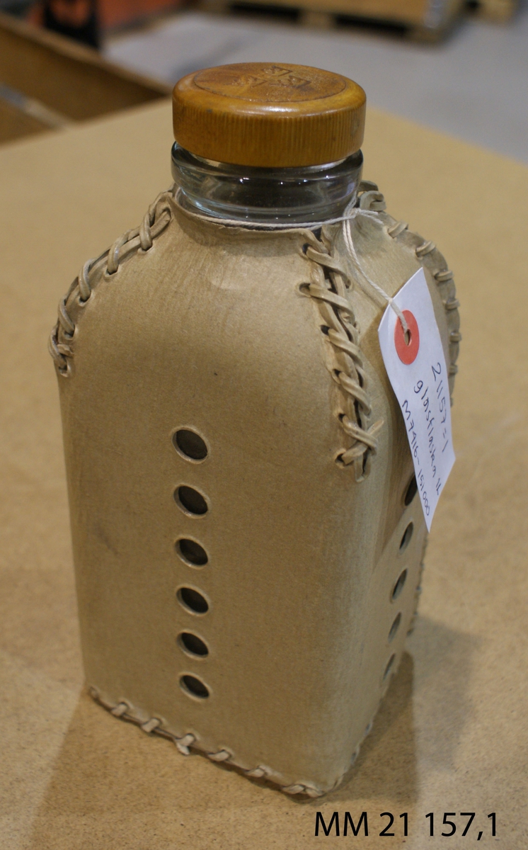 Flaska av glas, fyrkantig formklädd i läderskydd. Gul skruvkork märkt med tre kronor.