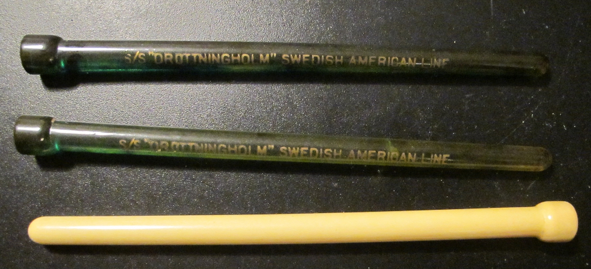 3 st drinkpinnar i benvit (1st) respektive transparent grönt. De två gröna med texten: "S/S "DROTTNINGHOLM" SWEDISH AMERICAN LINE". Föremålens form: Avlånga, runda