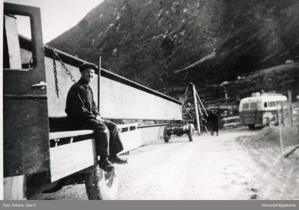 Olav E. Fekene transporterer jernbjelkane til Skøyten bru i Hemsedal i 1938.
Thomas Purkestad på lasteplanet. Lærdalsbussen på interimbrua.